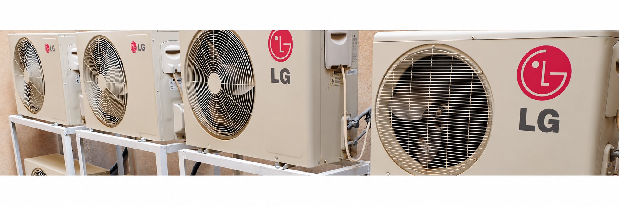 Plusieurs unités extérieures de climatisation de marque LG sont installées côte à côte sur des supports métalliques blancs contre un mur beige.