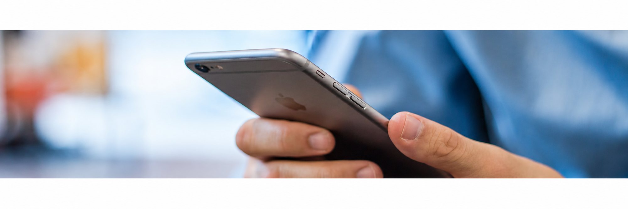 Gros plan sur deux mains qui tiennent un smartphone gris, avec un arrière-plan bleu et flou.