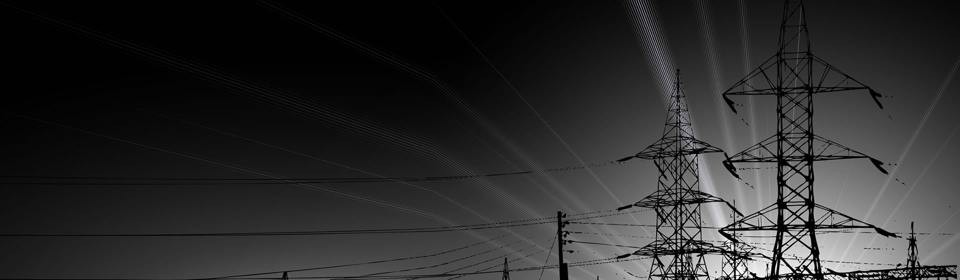 Silhouettes de pylônes électriques et de câbles à haute tension se détachant sur un ciel sombre, en noir et blanc.